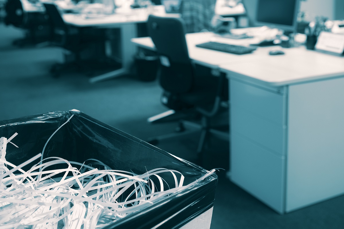 évitez les sanctions de la CNIL Papier déchiqueté dans une poubelle avec un espace ouvert flou et un bureau moderne en arrière-plan