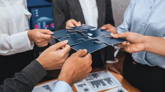 Des cadres et des employés travaillent ensemble au bureau, assemblant les pièces d'un puzzle avec des documents posés sur la table